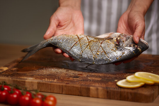 Chef hands holding seasoned sea bream ready for cooking