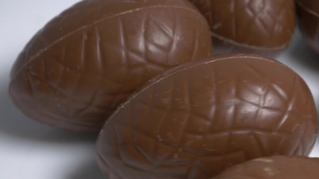 Close-up of milk chocolate Easter eggs rotating on a white plate, showcasing their textured pattern and glossy surface under bright studio lighting.