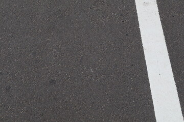 Fototapeta premium Asphalt road surface with white lane marking in close-up view. Minimalist transportation background, street pavement texture, road infrastructure detail, abstract urban pattern, civil engineering