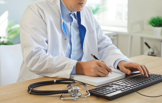 Close-up of man doctor or nurse writing prescription and working on computer with documents in clinic office, focusing on research in a professional setting with attention to detail.
