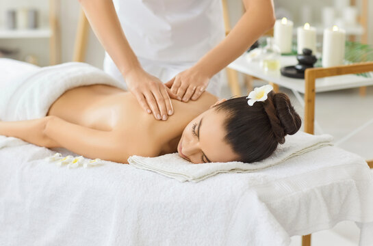 Woman receives relaxing back massage therapy at spa salon. Smiling client on a towel as therapist masseuse eases tension and fosters wellness in a calm clinic room. Beauty and body care concept.