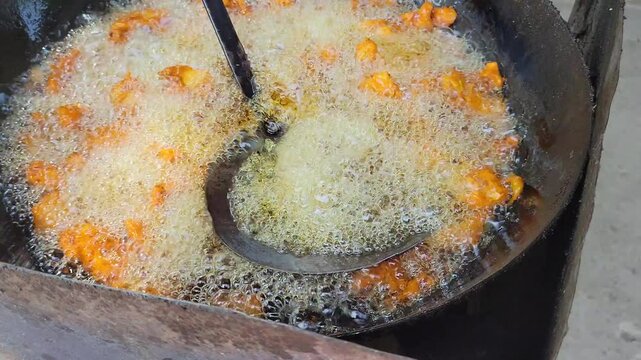 Deep frying traditional crispy vegetable pakoras in a large wok
