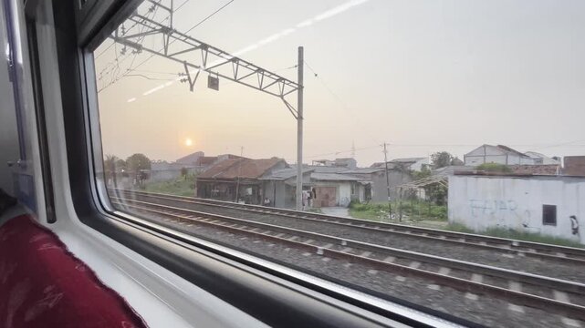 Scenic sunset viewed through a moving train window with railway tracks and urban landscape, conveying travel and peaceful commuting.