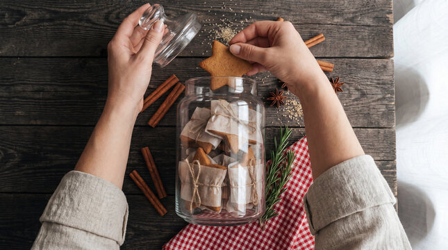 Hands placing a gingerbread cookie into a glass jar with Christmas treats