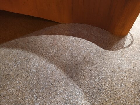 Abstract architectural background featuring a curved wooden wall, textured aggregate floor, and dramatic shadow play with ample B2B copy space.