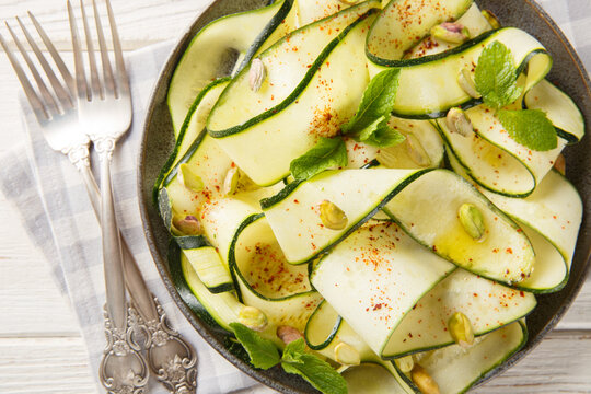 Gourmet zucchini ribbon salad with pistachios, chili pepper and mint, elegant vegetable appetizer close-up in a plate on the table. Horizontal top view from above