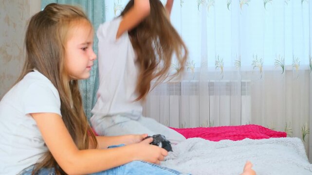 Carefree sisters playing online video game with joysticks in bedroom. Little girls relaxation after school