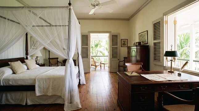 Vintage tropical bedroom with canopy bed, white mosquito netting and classic wooden desk with old maps