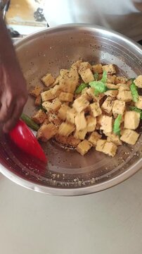 Chef mixing fresh Gujarati Dhokla with mustard seeds and green chilies in a steel bowl