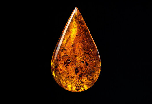 A single teardrop shaped piece of polished amber gemstone with visible organic inclusions isolated on a solid black background