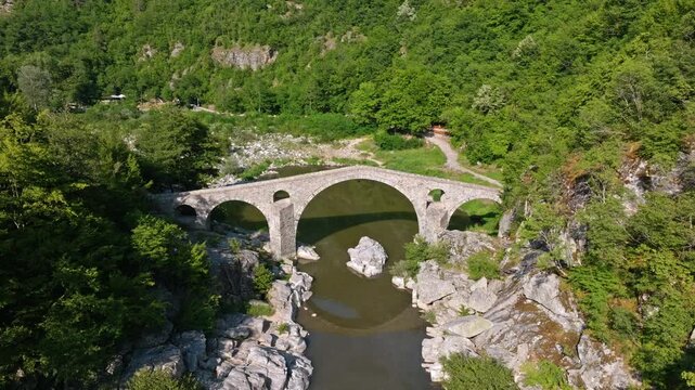 Dyavolski most Devils bridge crossing Arda river canyon high angle drone view ancient stone architecture lush green forest sunny daylight travel tourism landmark Bulgaria Rhodope mountains heritage.