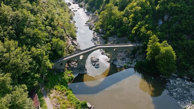 Arda river canyon Devils bridge side aerial drone view old stone arch shadow reflection mountain stream green forest bright sunny day travel destination Bulgaria Rhodope scenery.