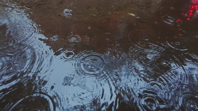 Close-up of Raindrops falling into an autumn puddle on cobblestone pavement. Natural background on rainy autumn day. Natural pattern of rain drops on puddle