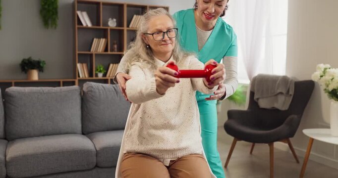 Senior woman physiotherapy exercise caregiver nurse homecare. She lifts a dumbbell as a nurse guides posture to build strength and balance at home. Concept: home rehabilitation care and support.