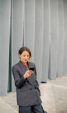 Woman using smartphone while standing near gray wall in urban setting