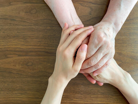 Young hands gently holding an elderly person's hands