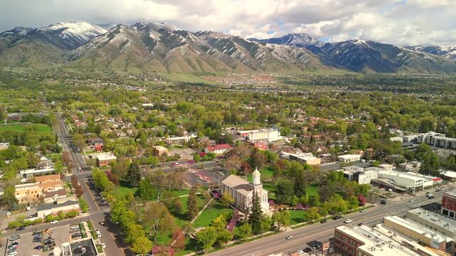 Drone orbits clockwise around a historic church steeple surrounded by tree lined streets
