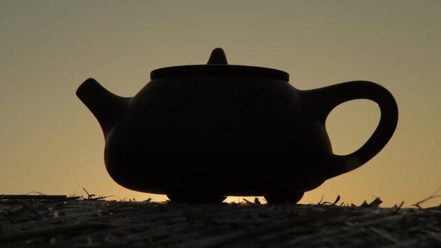 Silhouette of a traditional clay teapot against golden sunset light, useful for tea ceremony, mindfulness and Asian tea culture themes