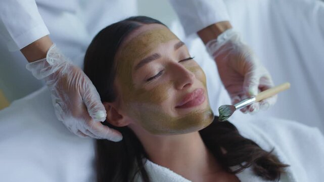 Woman lying peacefully with green clay mask on face in spa, 4K