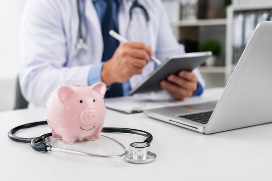Piggy bank with stethoscope and doctor using tablet background. Healthcare insurance cost, financial planning for medical expenses, and saving money concept .