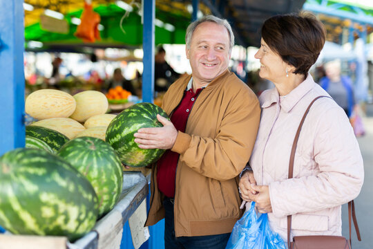 Cheerful elderly casual male and female picking fresh organic watermelon at local market