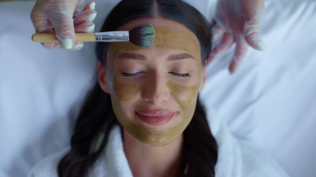 Closeup of young woman receiving green clay mask application at spa, 4K