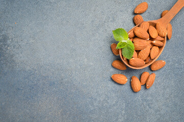 Organic raw almonds are placed in a wooden spoon. Fresh mint leaf decorates the nuts. Healthy snack provides energy. © Yaruniv-Studio