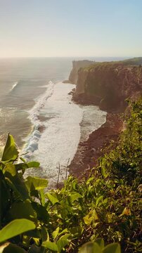 Vertical video. Slow Motion Coastal Panorama Of Karang Boma Cliff With Sunlight Reflecting Across Ocean Waves, Nature Travel And Exploration