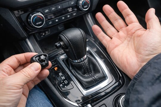 A person holding their hand up to the gear shift in a car, ready to drive