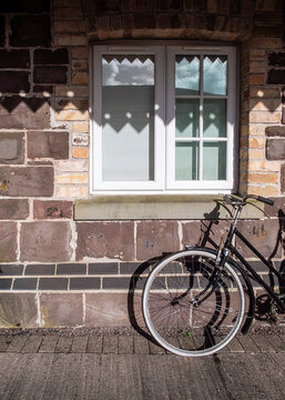 A vintage bicycle rests against a rustic stone wall beneath a white-framed window, evoking a quiet, stationary moment in time.
