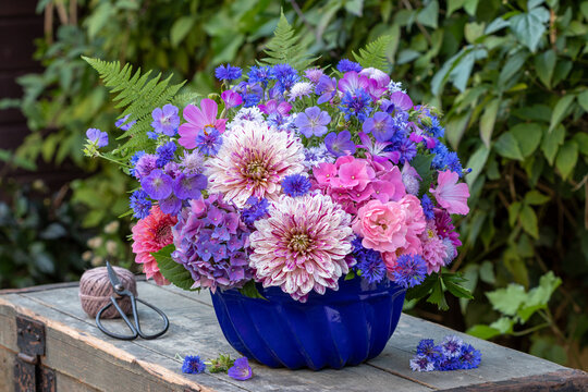 Blumen-Arrangement mit Dahlien, Rosen, Hortensienbl&uuml;ten, Federnelken, Wiesenstorchschnabel in alter Gugelhupfform im Sommergarten