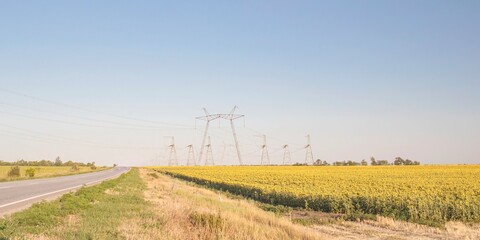 Obraz premium High voltage power lines over rural landscape with road and fields. Power pylons in rural area during harvest season.