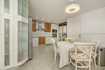 Obraz premium Traditional kitchen and dining area featuring cream cabinets with frosted glass doors, wood-accented lower units, stainless steel appliances, a round table 