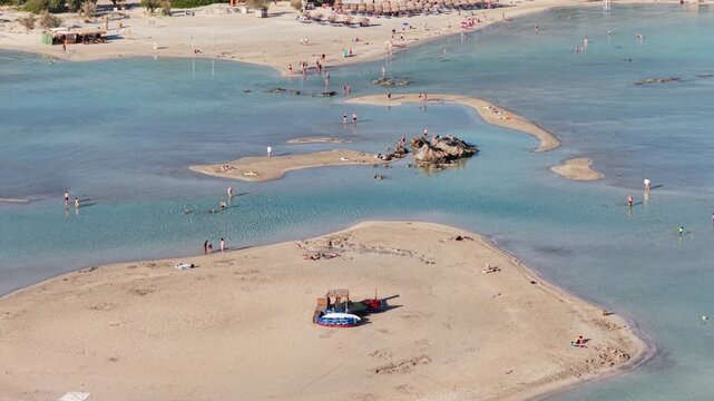 Aerial drone view of shallow turquoise water with sandbars and a large rock outcrop in the lagoon, Elafonissi, Greece