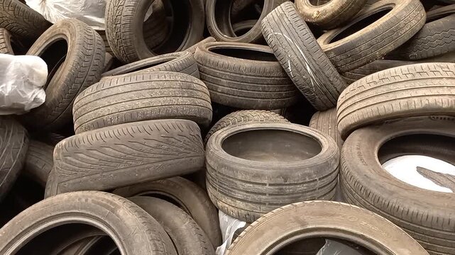 Large pile of used old worn car rubber tires dumped at outdoor landfill polluting environment representing hazardous automotive industry waste material and need for proper recycling disposal method