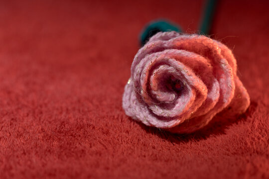 Solitary pink knitted flower on deep red, craft and coziness concept