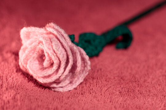 Single knitted pink rose on red surface, handmade textile art