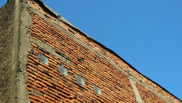 Unfinished red brick wall against a clear blue sky background.