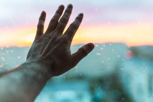 Reaching Hand Against Rainy Glass with Sunset Sky Behind