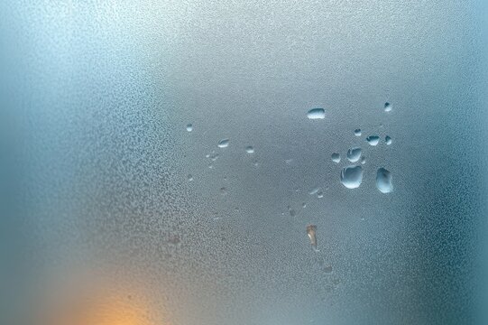 condensed frosted glass with scattered water droplets, blurred blue-gray background and soft warm glow, calm reflective mood