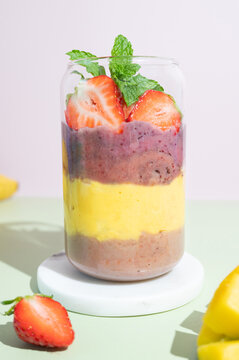Close up of colorful berry smoothie served in a glass with fresh strawberry garnish.