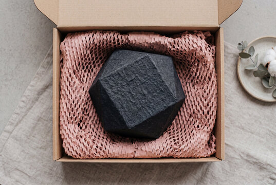 Geometric black coal soap bar or handmade concrete craft decor piece beautifully packed in a cardboard gift box with soft textured pink protective paper net wrapping material.