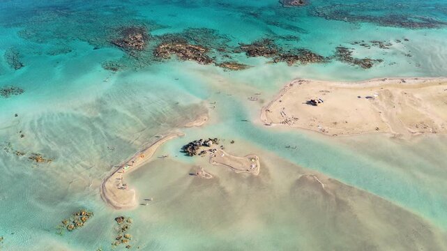 Overhead aerial drone view of pale sandbars and dark rocks scattered across a shallow turquoise lagoon, Elafonissi, Greece