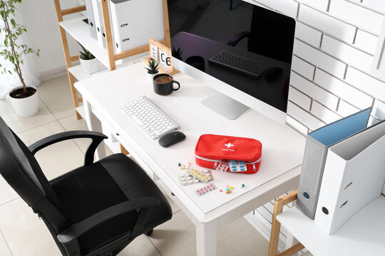 First aid kit with various pills and medications on a white office desk with computer and chair