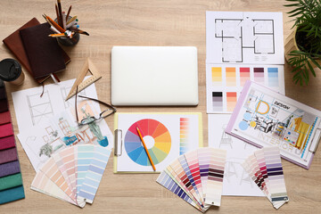 Interior designers wooden desk with laptop, color palettes, fabric samples, and architectural plans, top view
