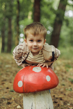 Cute little boy hiding behind decorative wooden mushroom in forest