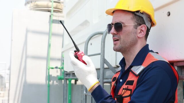 Male technician inspects the coolant inlet and outlet pipes of the cooling tower checks the flange connections and reports walkie talkie engine room while testing the cooling system.