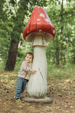 Cute little boy hugging a huge decorative wooden mushroom in forest