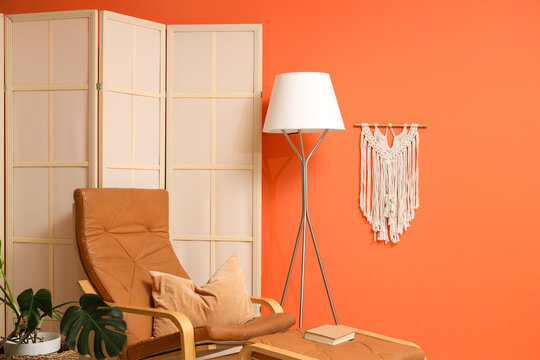 Interior of living room with folding screen, armchair and ottoman near orange wall