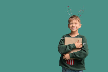 Obraz premium Cute little boy in Christmas reindeer horns with book on green background